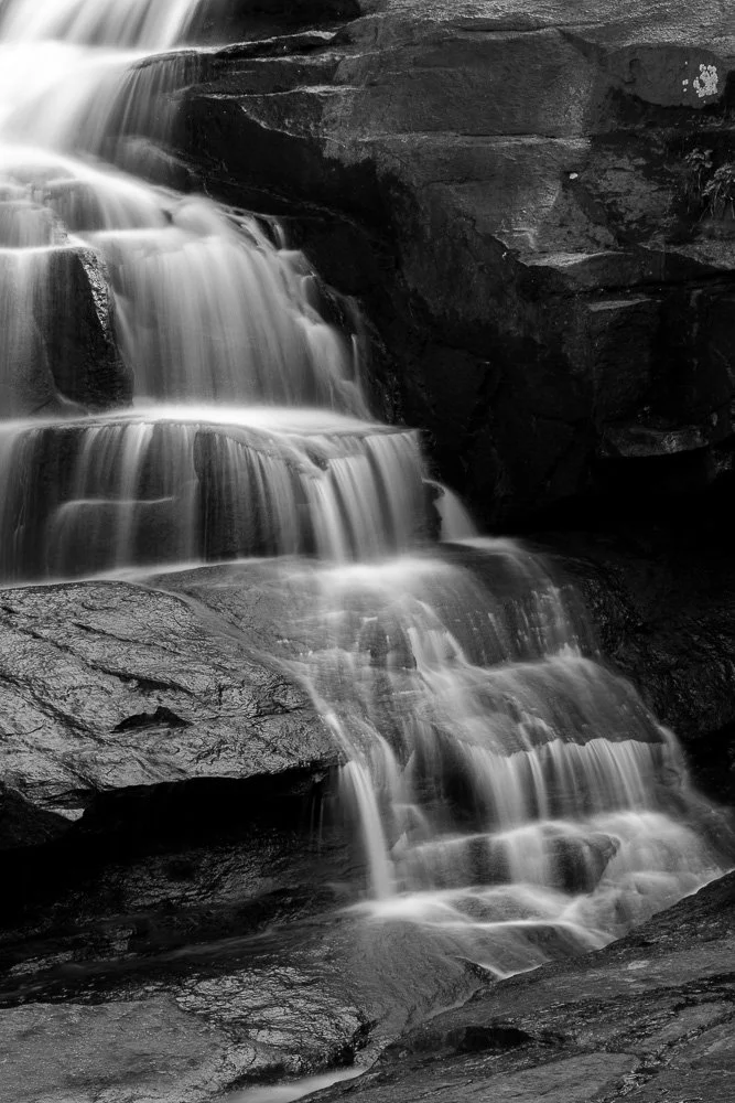 Black and white photo of a cascading waterfall over rocks.