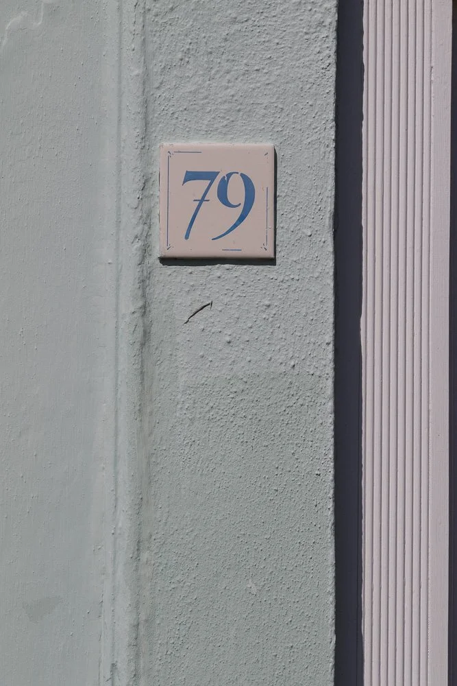 House number 79 on a light-colored textured wall with corner trim.
