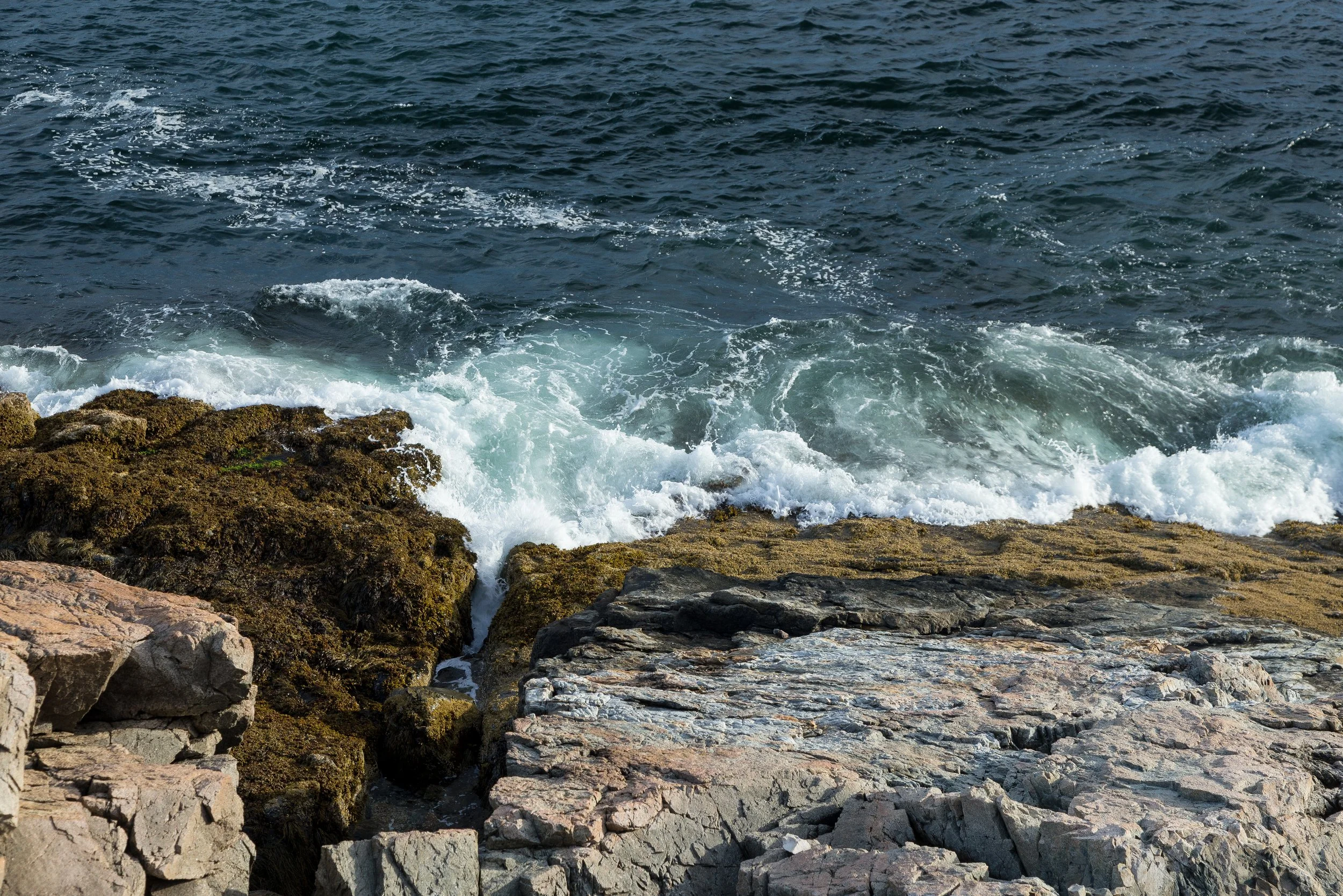 Rocks along the shoreline with ocean waves crashing against them.