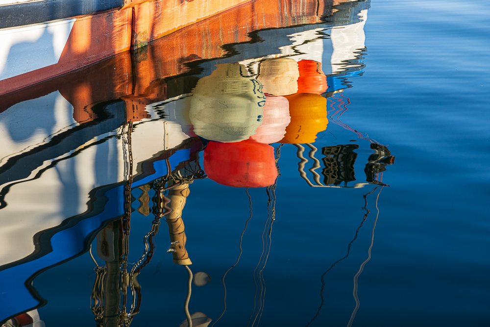 Colorful fenders hanging from a boat's side, reflected in calm water.