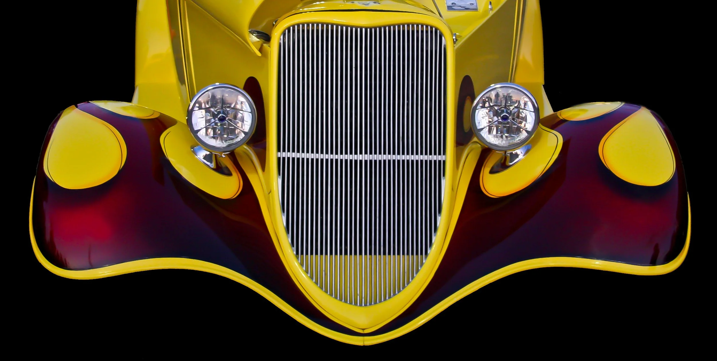 Front view of a vintage yellow race car with red and purple flame detailing, featuring a prominent grille and round headlights.