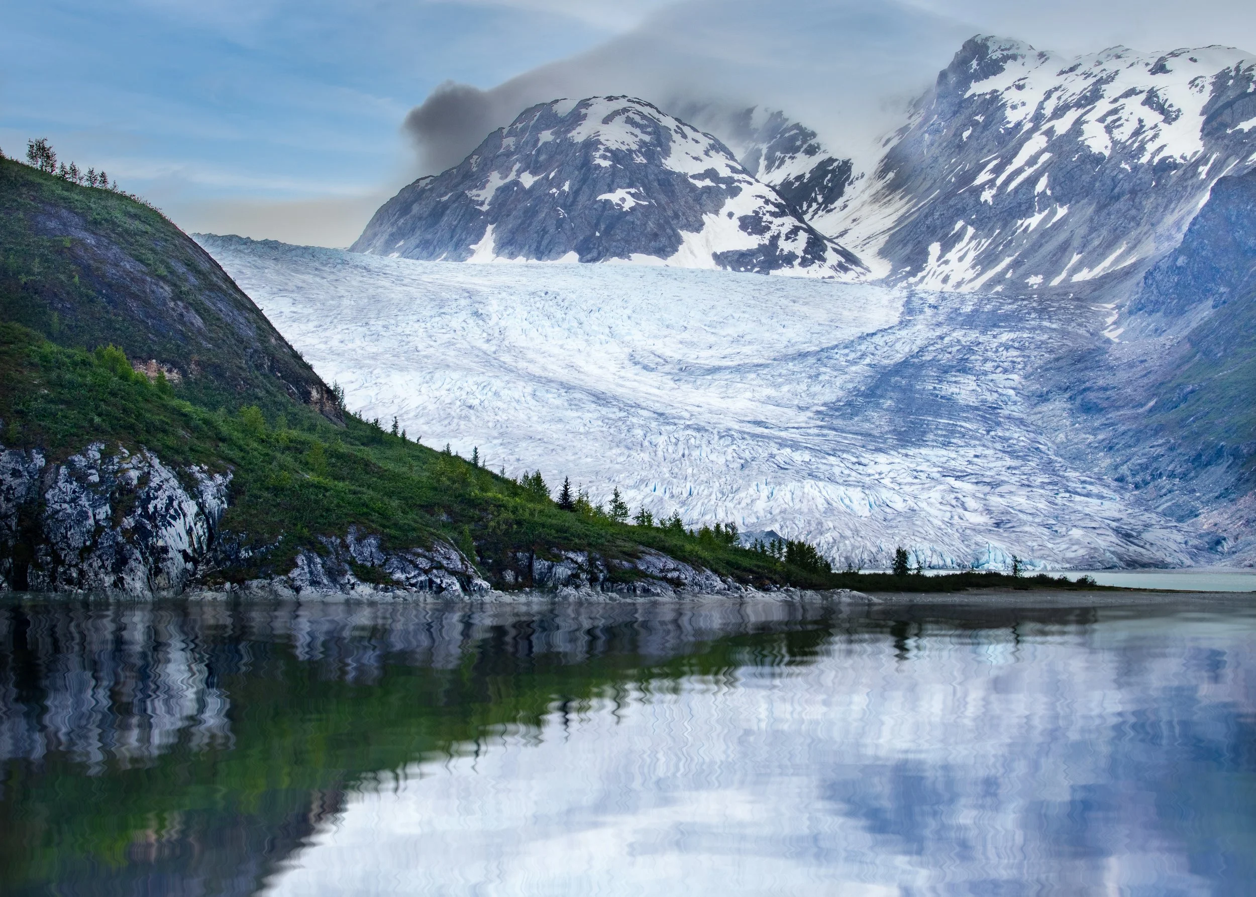 A scenic view of snow-capped mountains, a glacier, and a reflective body of water in the foreground. Alaska