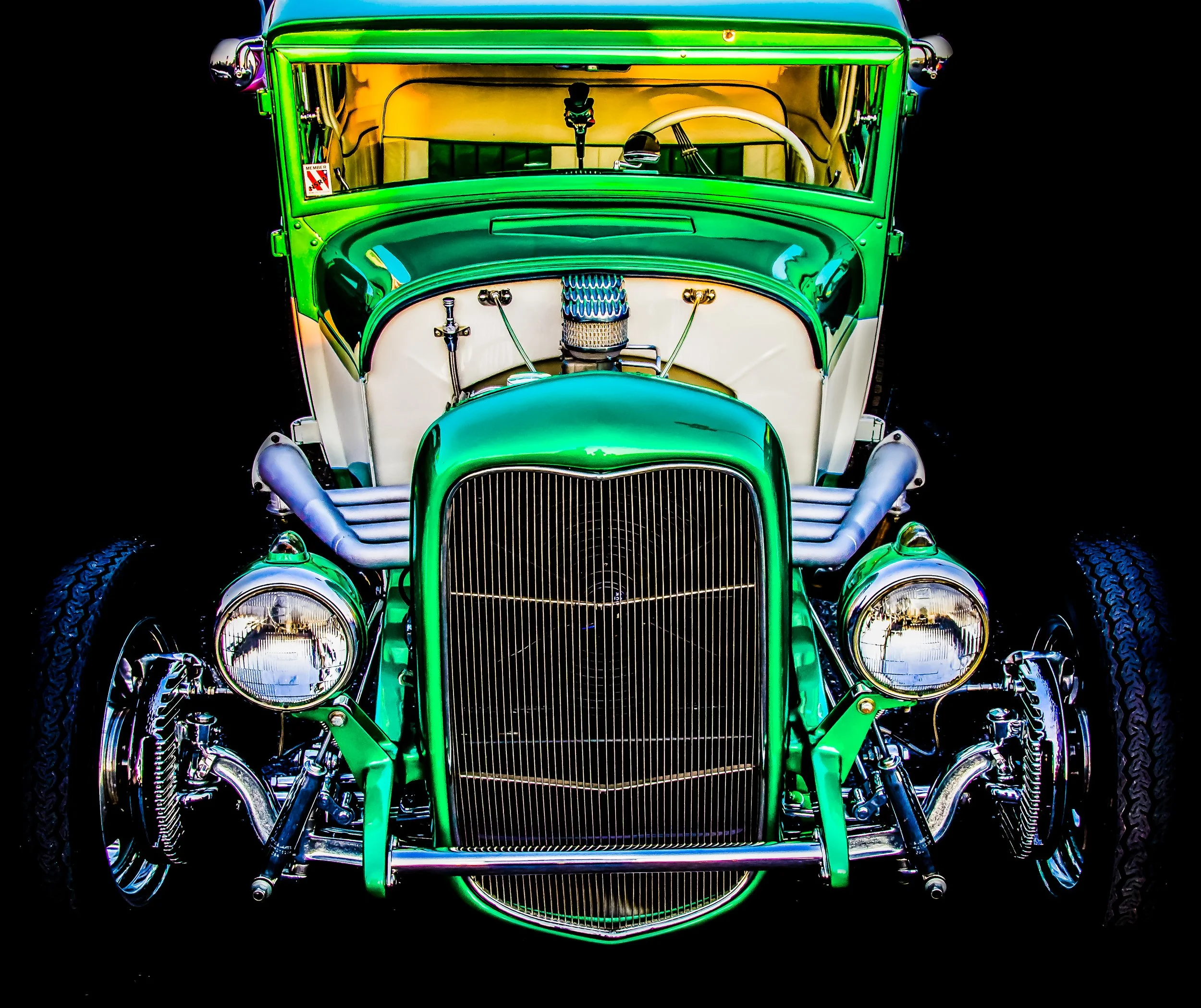 Front view of a vintage green and white hot rod car with chrome details and large headlights, isolated on a black background.