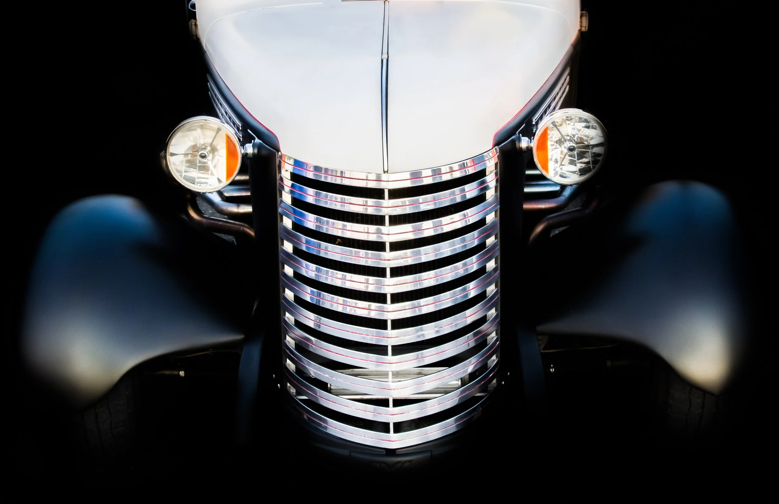 Front view of a vintage car with rounded headlights, a prominent vertical grille with horizontal chrome bars, and curved fenders.