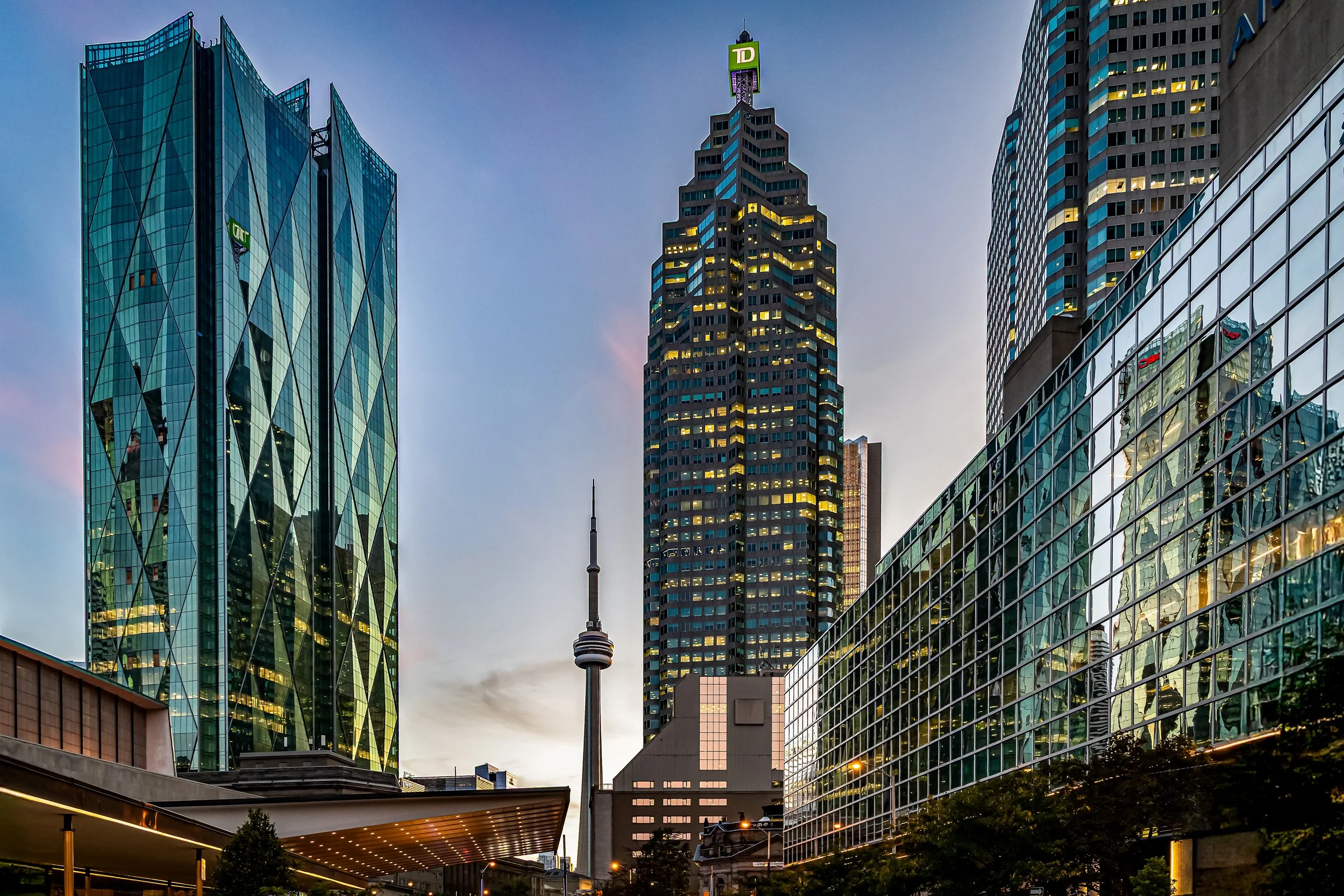 Cityscape of downtown Toronto with tall modern buildings, the CN Tower, and the TD Building at dusk.