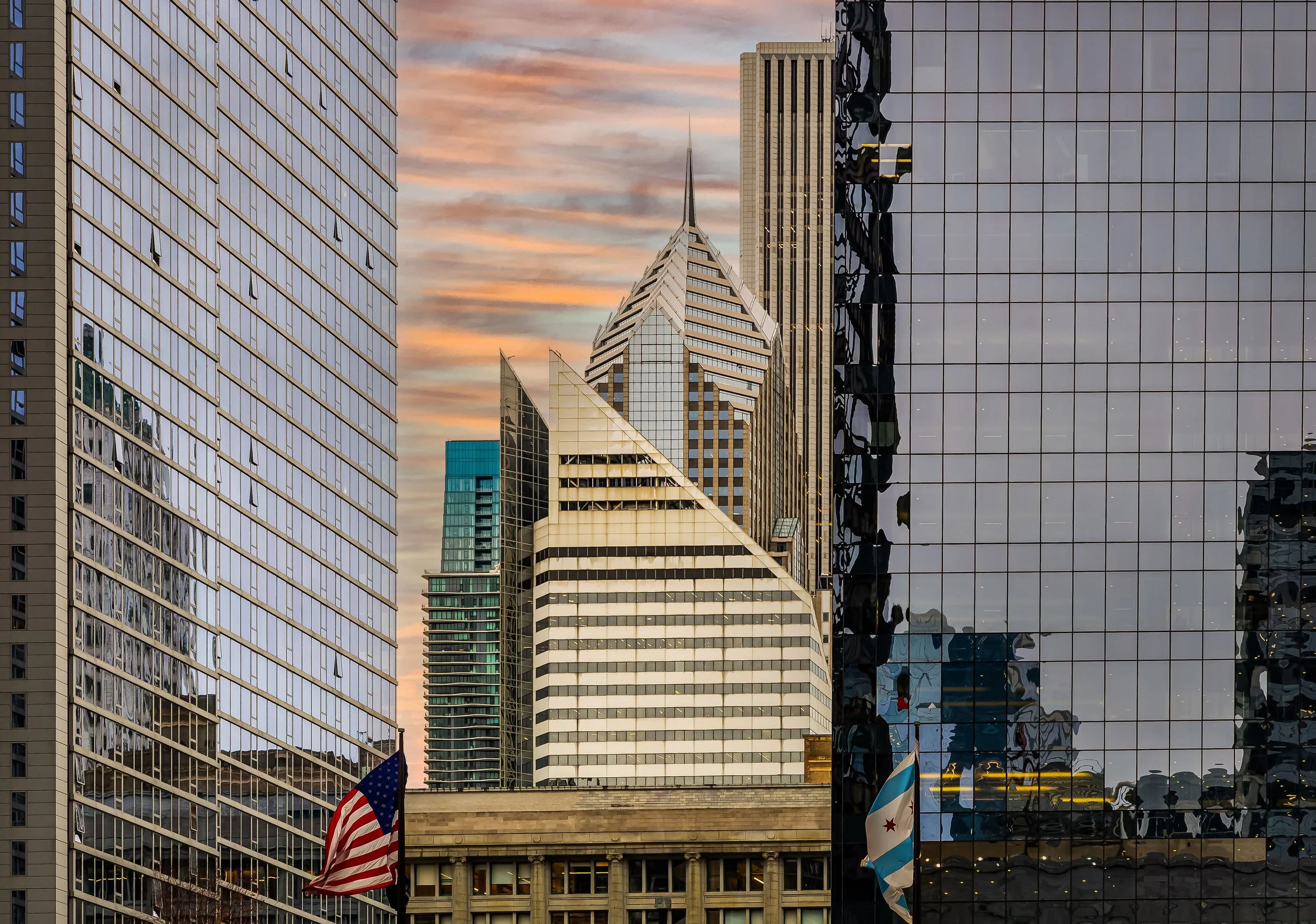 City skyline with modern glass skyscrapers during sunset, including the Wrigley Building and American and Chicago flags in the foreground.