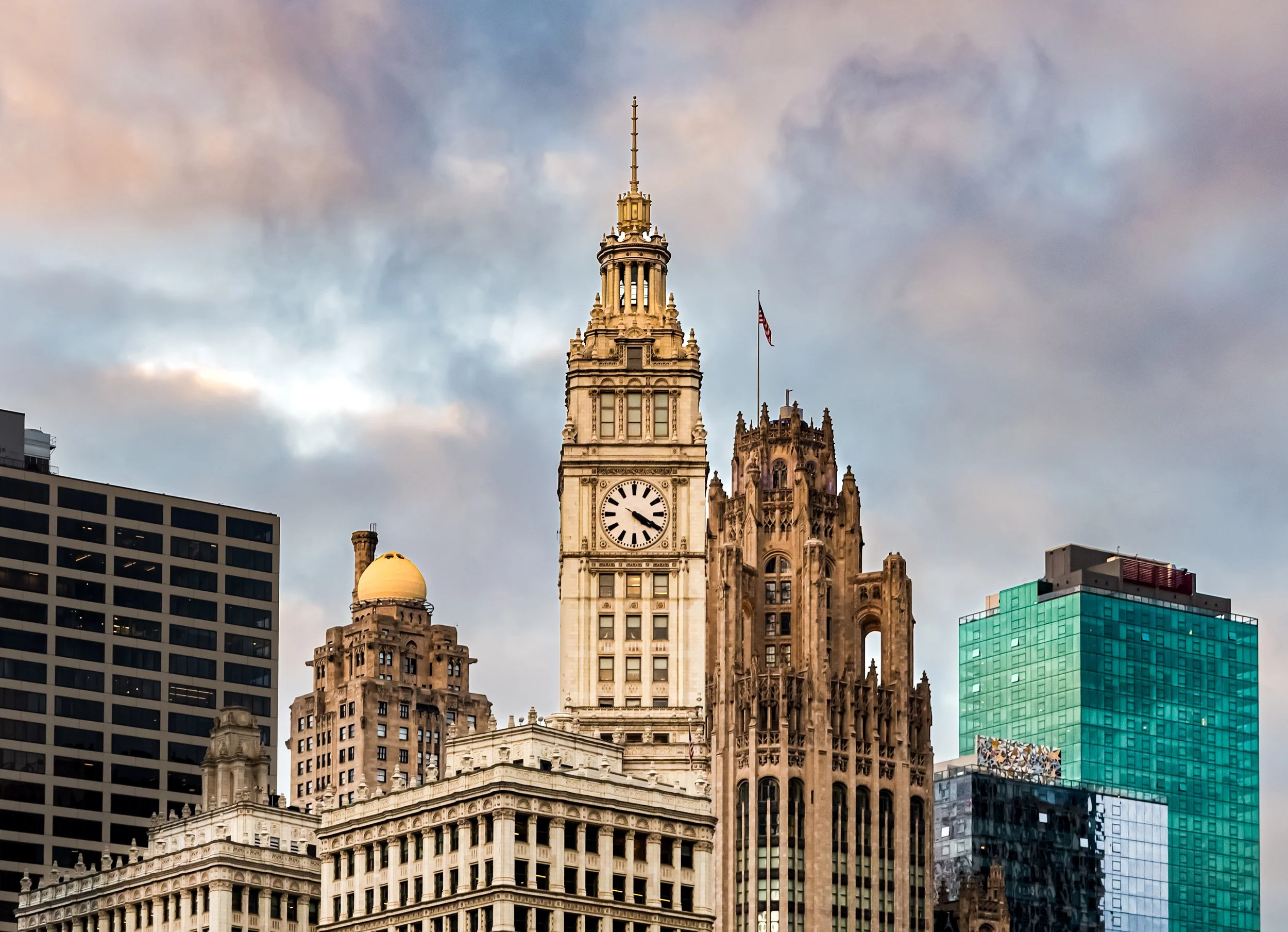 Cityscape with tall historic clock tower and surrounding modern buildings under cloudy sky.