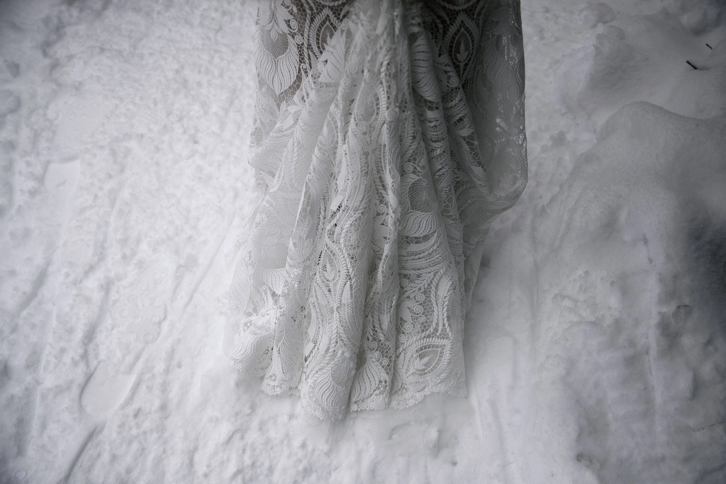 Close-up of a white lace wedding dress on snow at Golden Creek Pond in Snoqualmie Pass, Washington. Photographed by Megan Farmer, documentary style wedding photographer based in Seattle, Washington. 