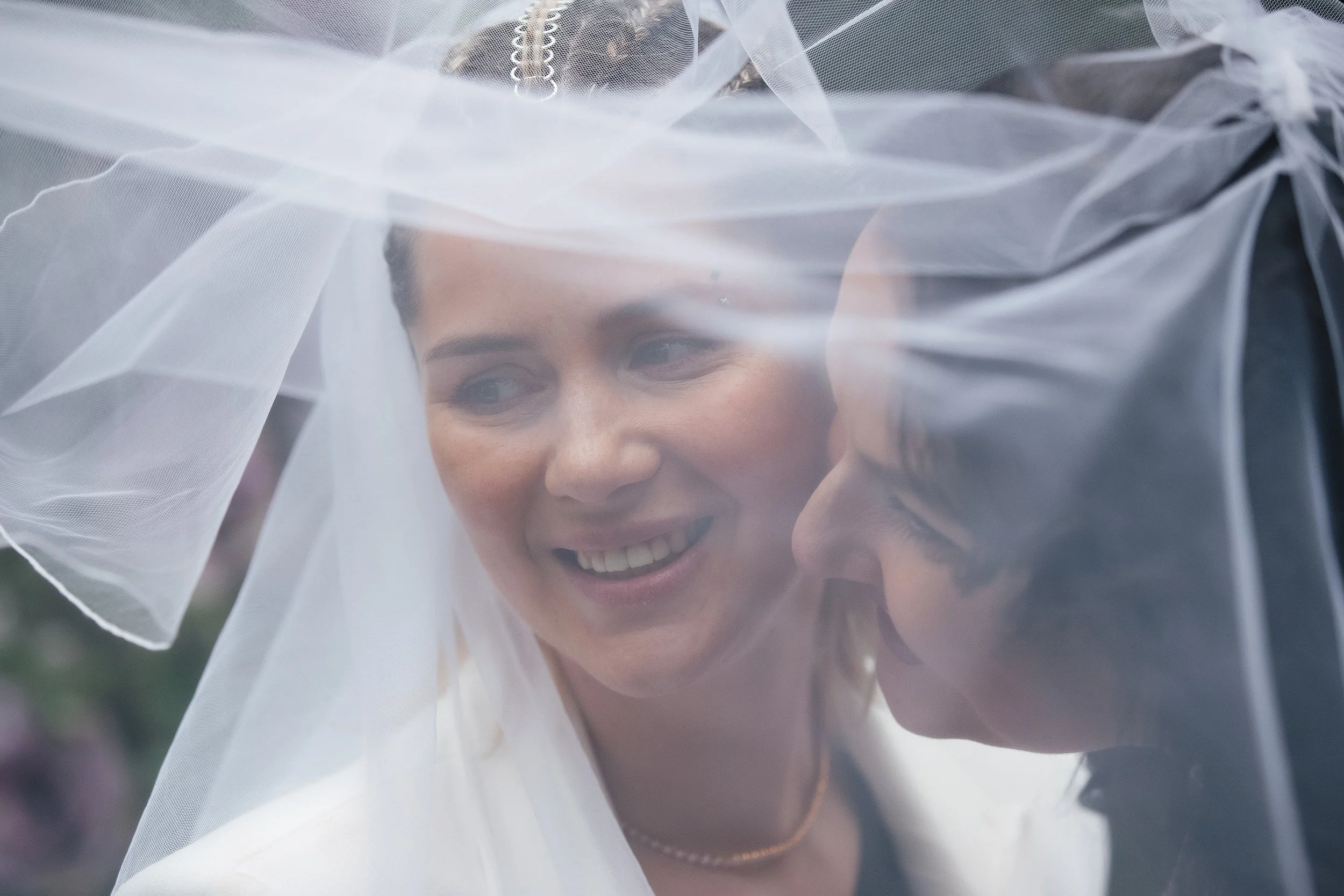 Brides share a moment under a veil while taking photographers following their wedding ceremony, photographed by Megan Farmer, a documentary style wedding photographer based in Seattle, Washington. 