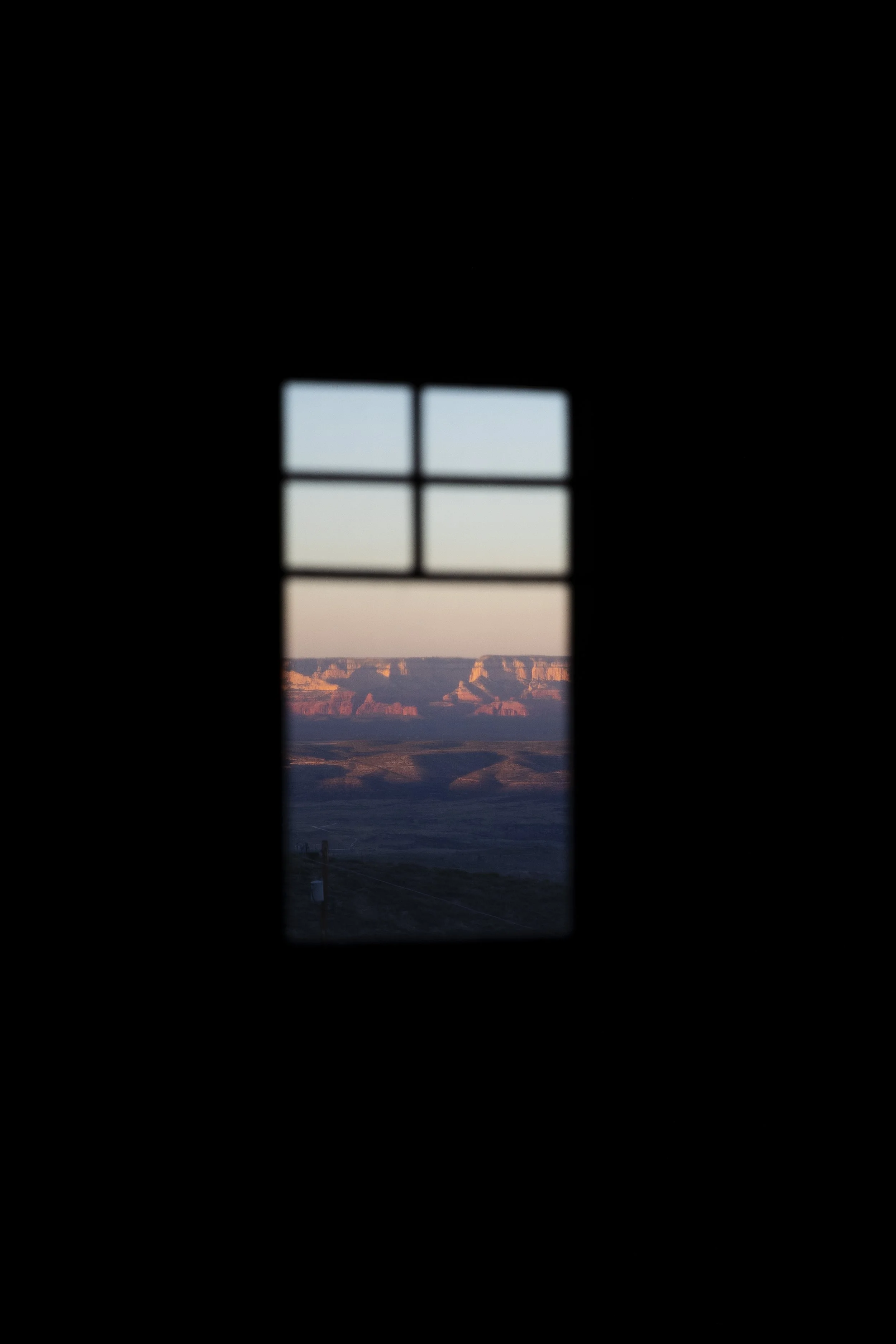 A view of an Arizona landscape is shown  through a small window with four panes at sunset, at the Little Daisy, a wedding venue in Jerome, Arizona. Photographed by Megan Farmer, a documentary style wedding photographer based in Seattle, Washington. 