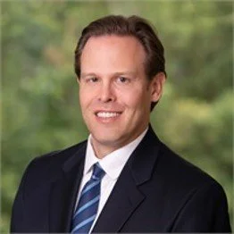 Portrait of a man in a suit against a blurred green nature background.