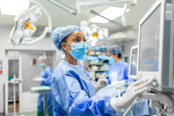 A team of healthcare professionals in surgical scrubs and masks working in an operating room with medical equipment and monitors.