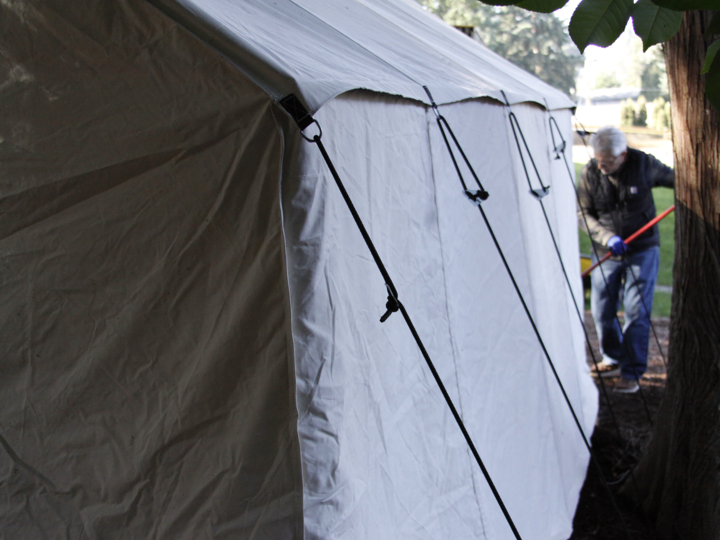 Man setting up a large white tent outdoors with trees and grass in the background.