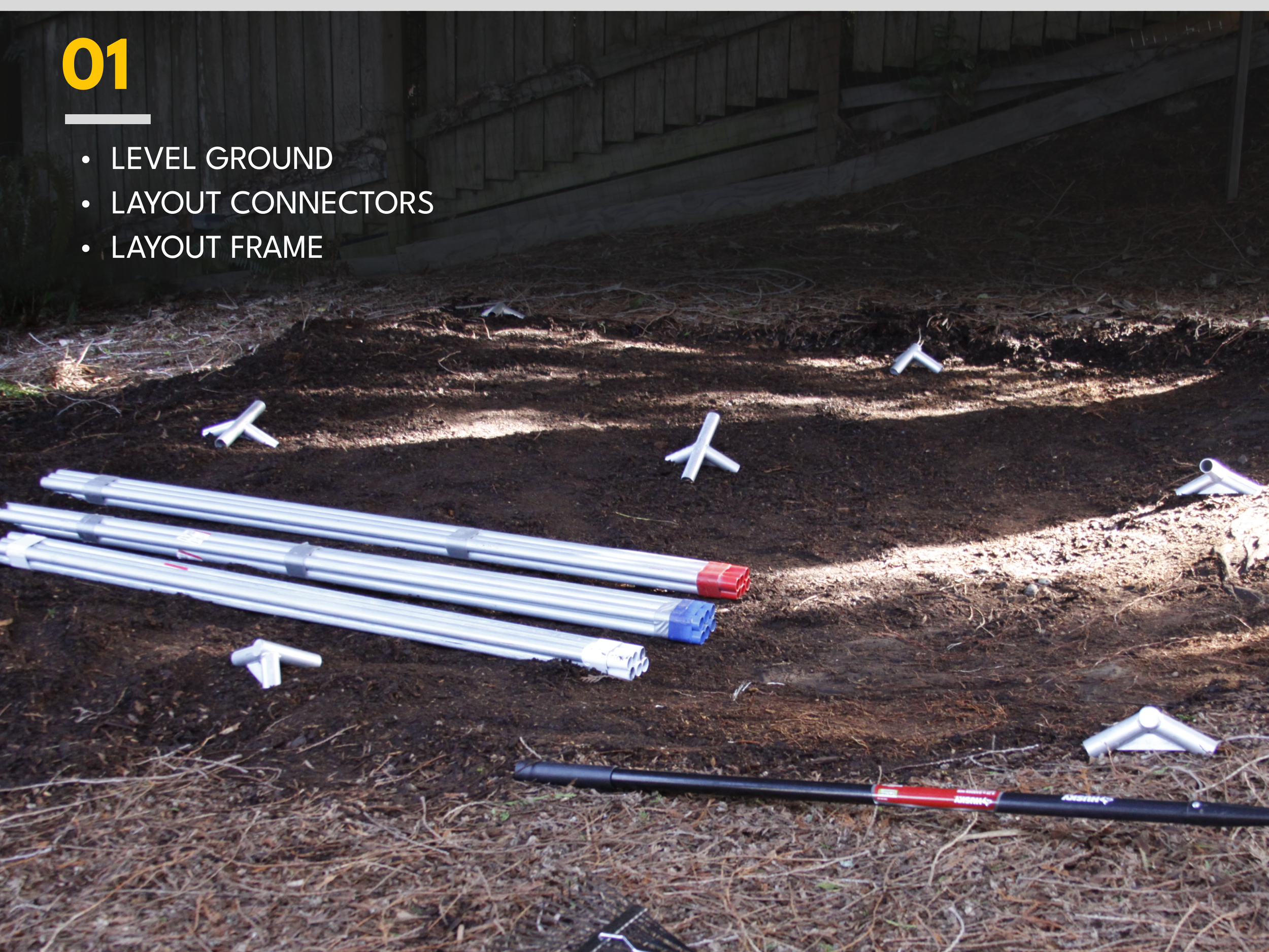 Construction site with plumbing pipes and connectors laid on dirt area, with wooden fence in the background.