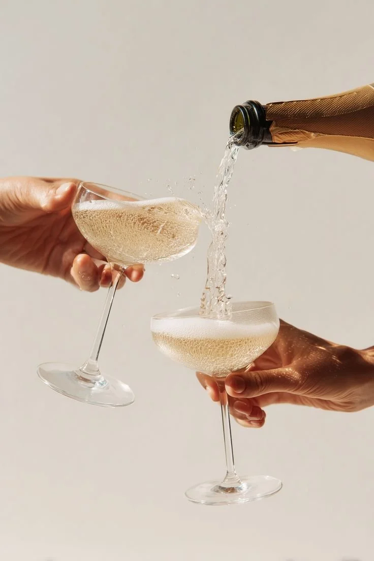 Two hands holding champagne flutes, with one hand pouring champagne into the other.
