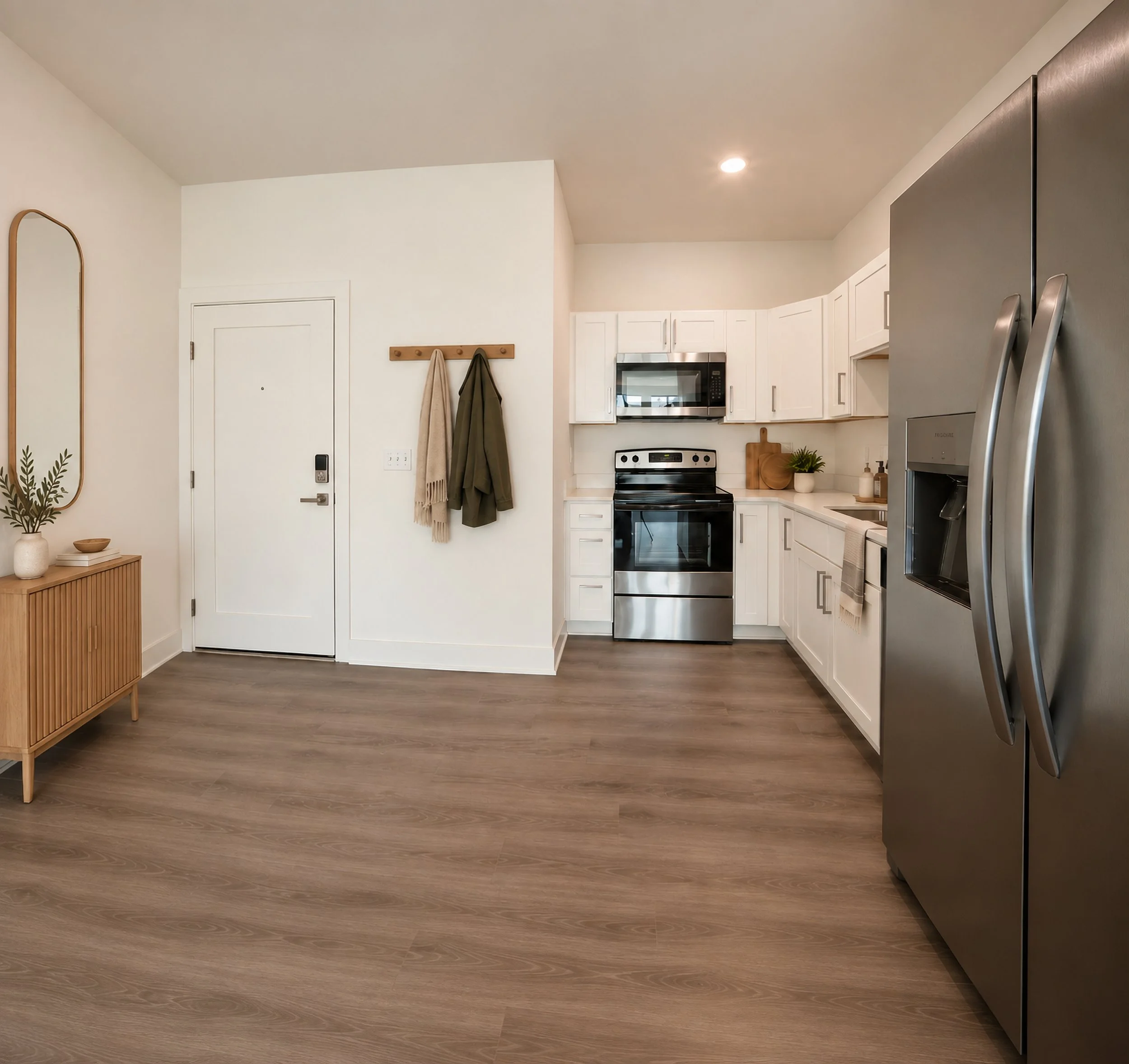 Virtually staged modern kitchen with white cabinets, stainless steel appliances, and light wood flooring. There is a entry door with a wooden coat rack holding two coats. A small wooden side table with decorative items is visible.