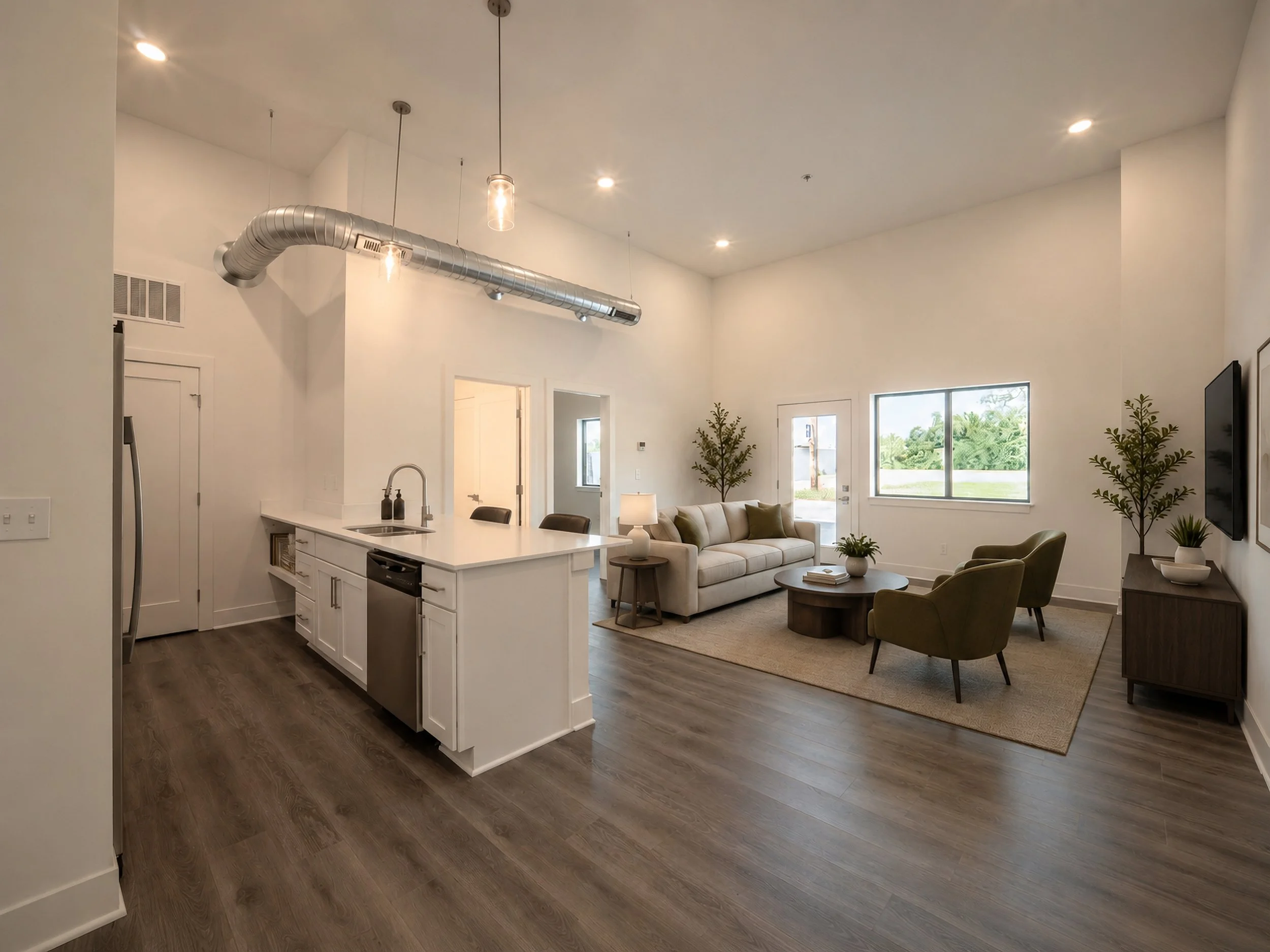 Virtually staged living room and kitchen with white walls, dark wood floors, a beige sofa, green armchair, coffee table, plants, flat-screen TV, large windows, and modern lighting fixtures including a metallic duct ceiling feature.