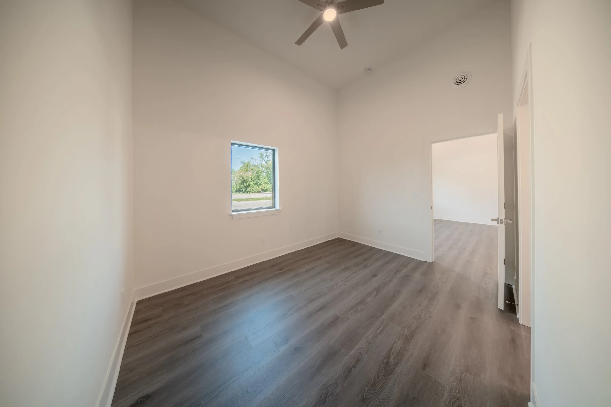 Empty room with white walls, a window, a ceiling fan with light, and wood-look flooring.