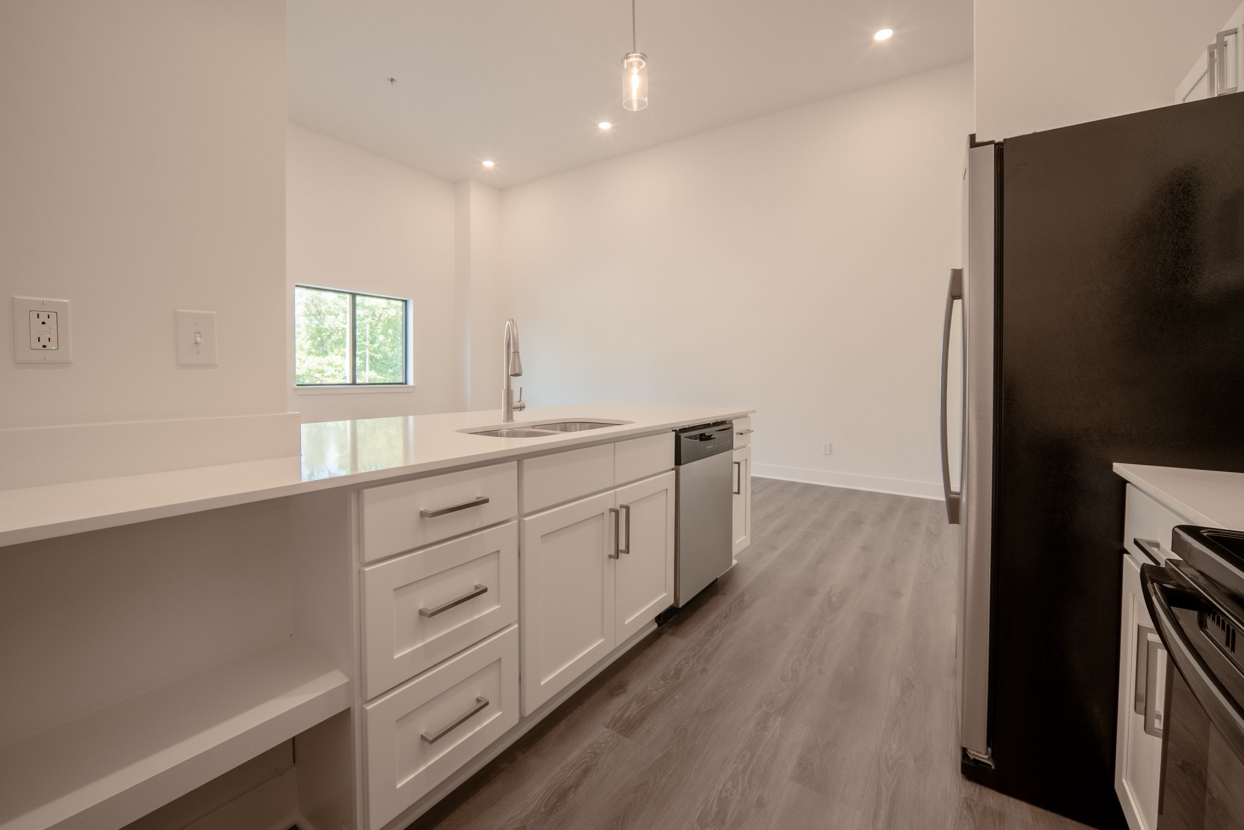 Modern kitchen with white cabinetry, stainless steel appliances, a black refrigerator, a window showing greenery, and wood flooring.