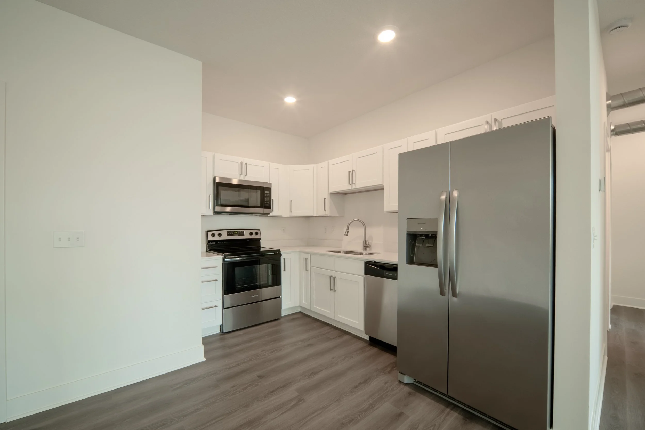 A modern kitchen with white cabinets, stainless steel appliances, dark wood flooring, and a stainless steel refrigerator.