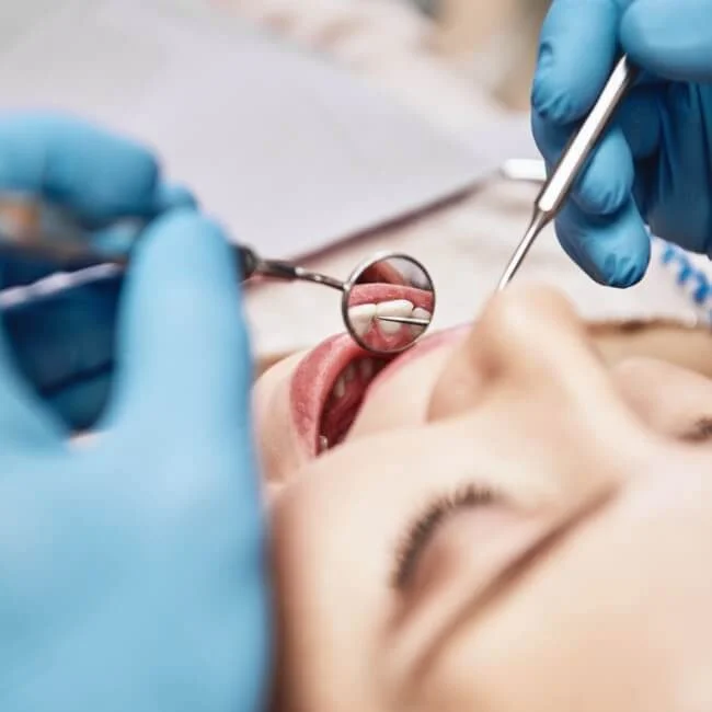 Dentist's hands holding dental tools near a patient's open mouth