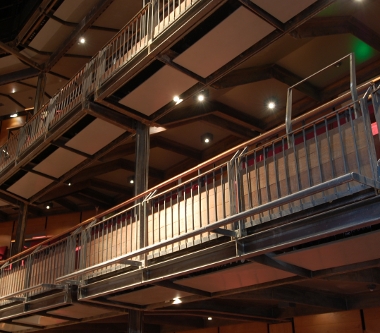 Interior of a multi-level industrial-style building with metal railings and exposed ceiling beams, illuminated by ceiling lights.