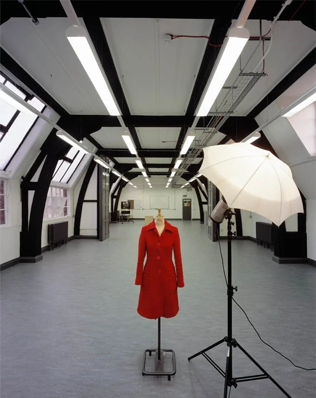 Art and Photography Studio with a mannequin wearing a red coat in the center, and photography equipment including a white umbrella and studio light to the right.
