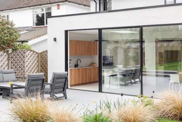 Modern backyard with outdoor seating area, a view of the kitchen through large glass sliding doors, and a landscaped garden with ornamental grasses.