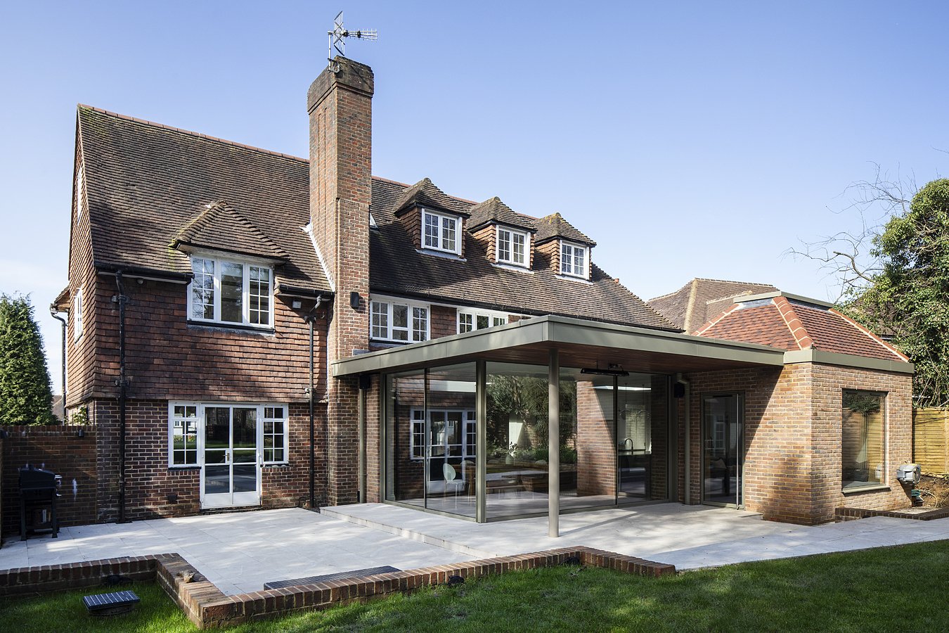 Backyard view of a brick house with a modern glass extension and a patio area.