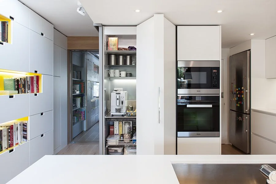 Modern kitchen with built-in appliances, white cabinets, stainless steel refrigerator, and open shelving with dishes and storage containers.