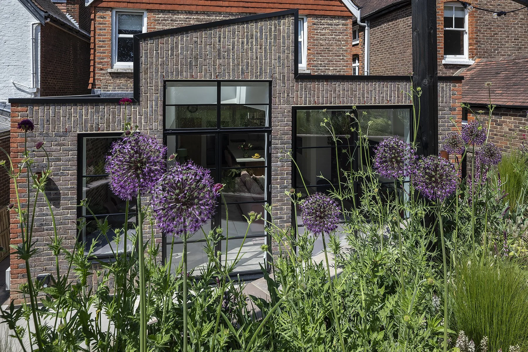 Extension building with large windows and brick facade, surrounded by purple flowering plants and greenery.
