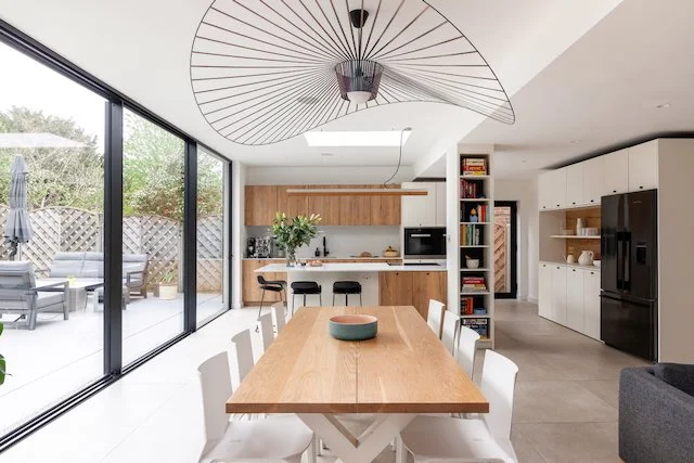 Modern dining area and kitchen with wooden accents, white cabinets, black appliances, and large glass sliding doors leading to outdoor patio.
