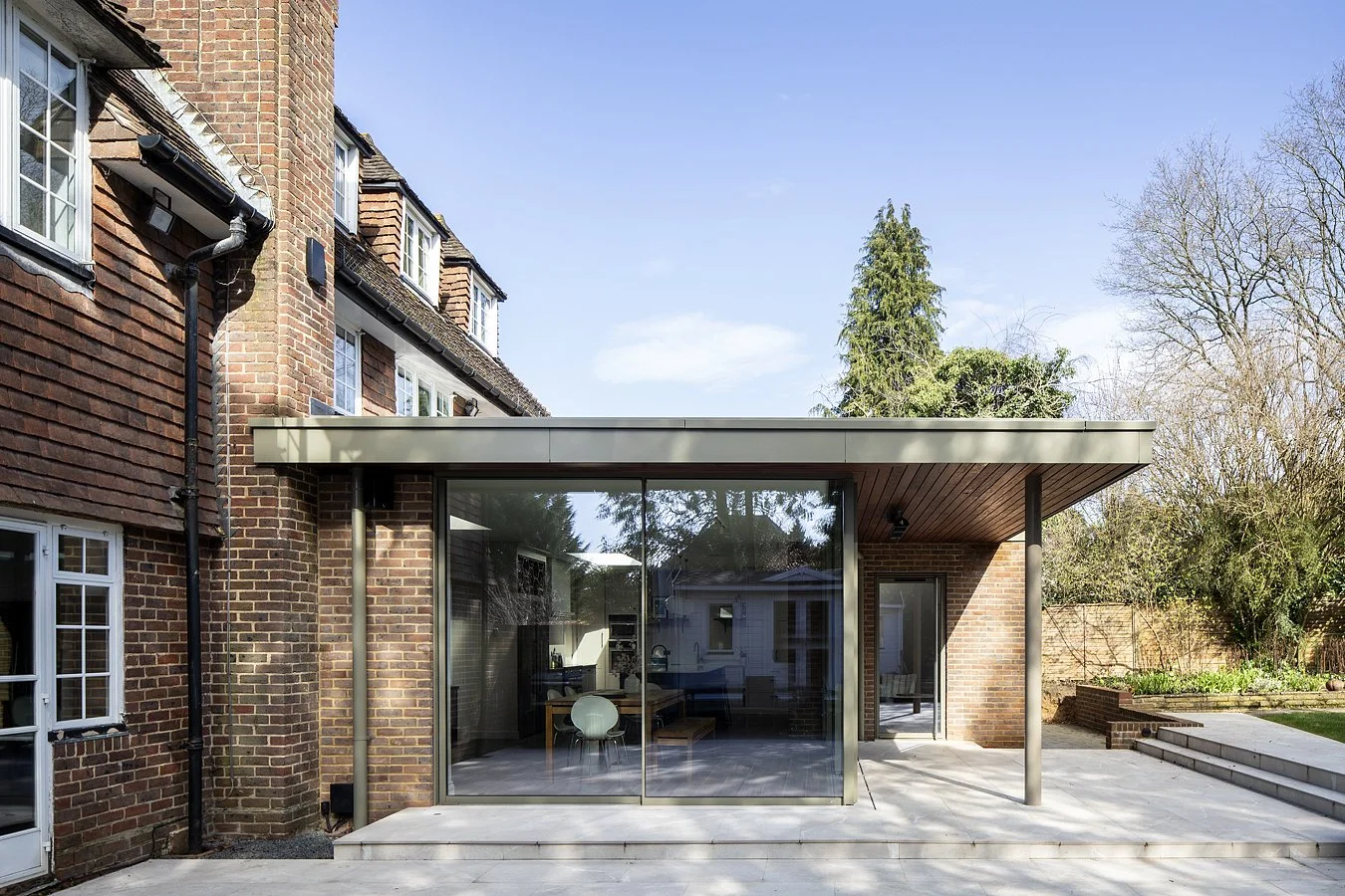 Modern glass extension attached to a brick house with outdoor patio and garden.