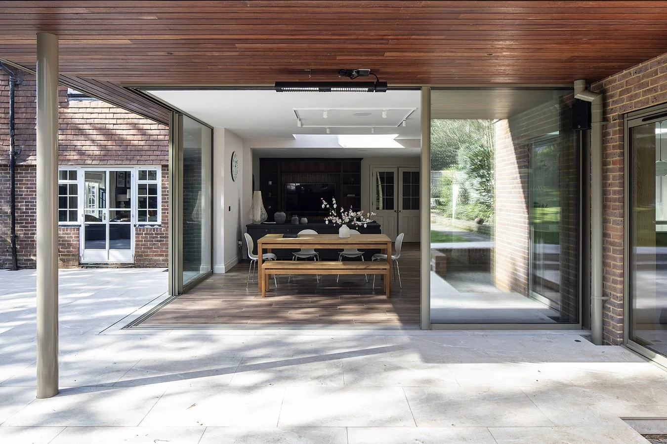 Modern dining room with wooden table, chairs, and a floral centerpiece, open to outdoor patio through sliding glass doors
