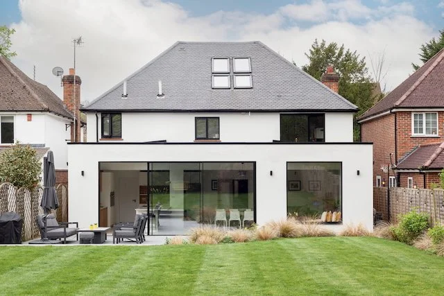 Modern two-story house with large glass sliding doors, a balcony, and a landscaped backyard.