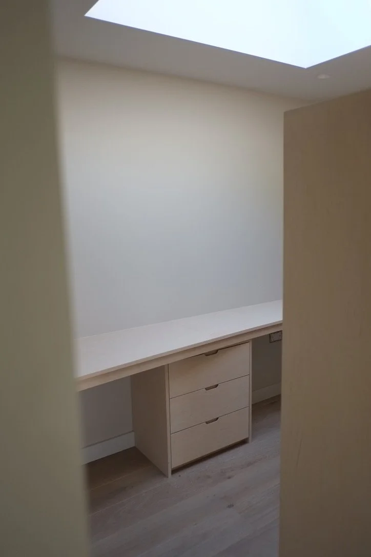 A small room with a built-in desk and a set of drawers beneath it. The room has a skylight in the ceiling, allowing natural light to enter.