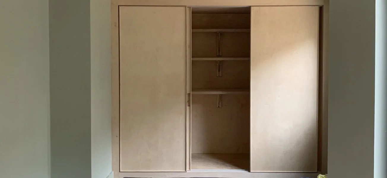 Empty wooden closet with sliding doors, open to reveal shelves inside.