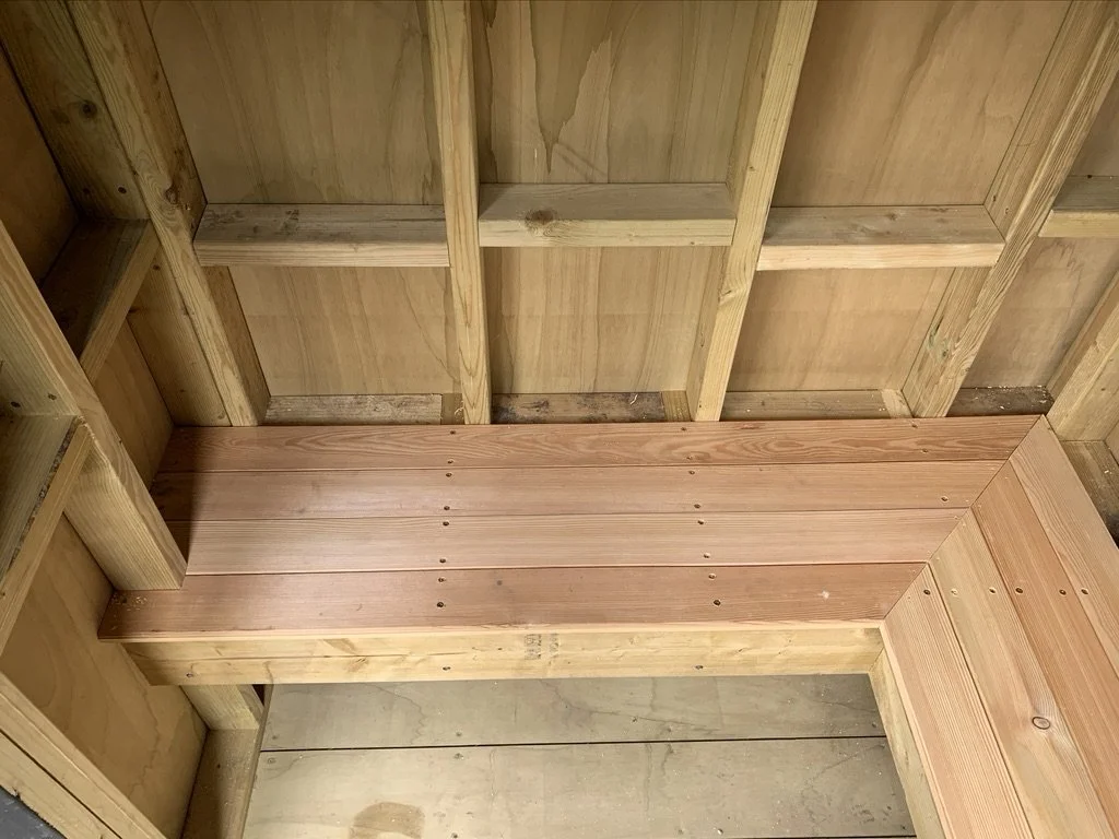 Interior of a wooden structure with unfinished walls and a wooden bench or platform.