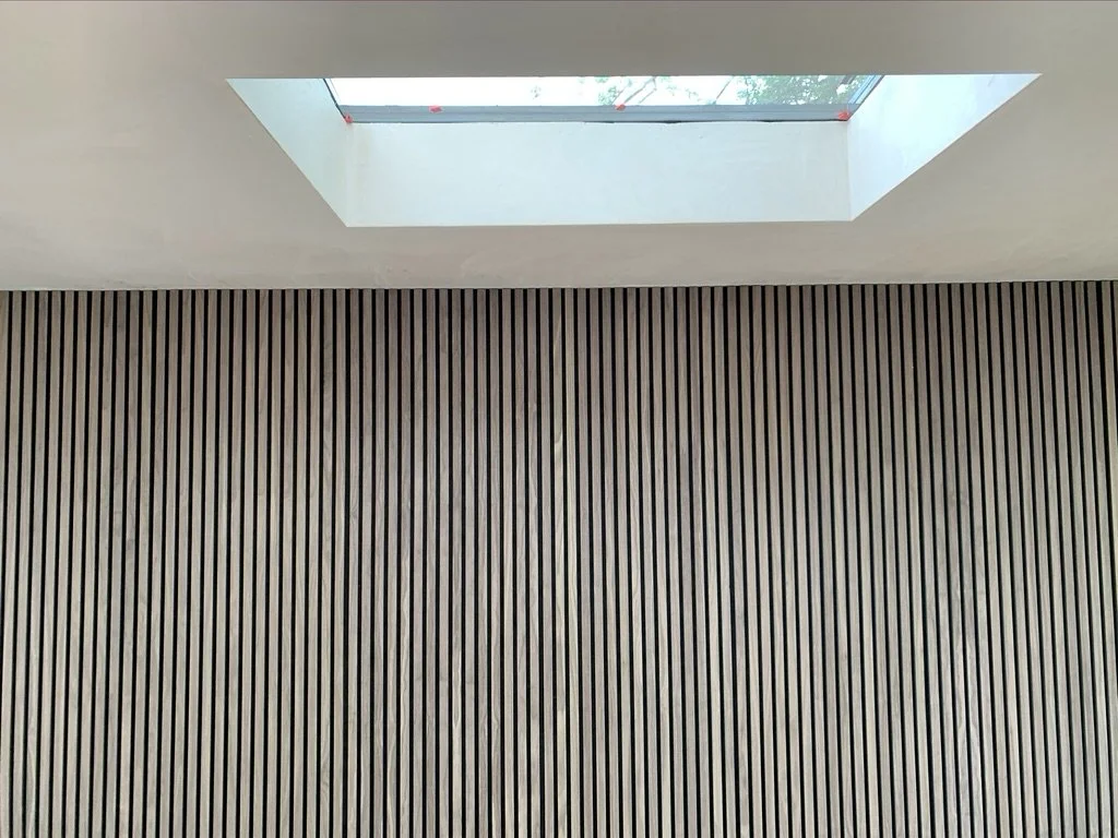 Interior view of a room with a wooden slat wall and a rectangular skylight letting in natural light.