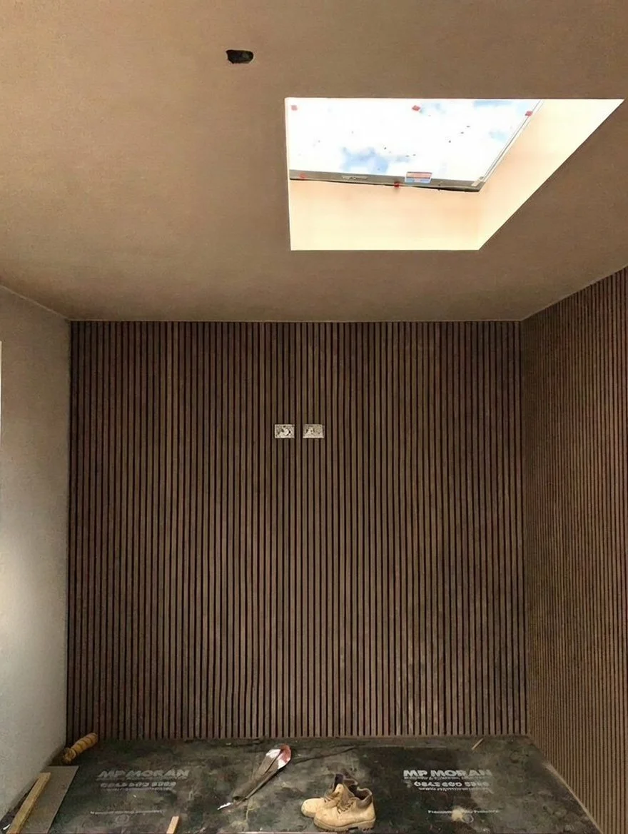 Interior room with wood-paneled wall, construction tools and shoes on floor, and a skylight in the ceiling showing blue sky and clouds.