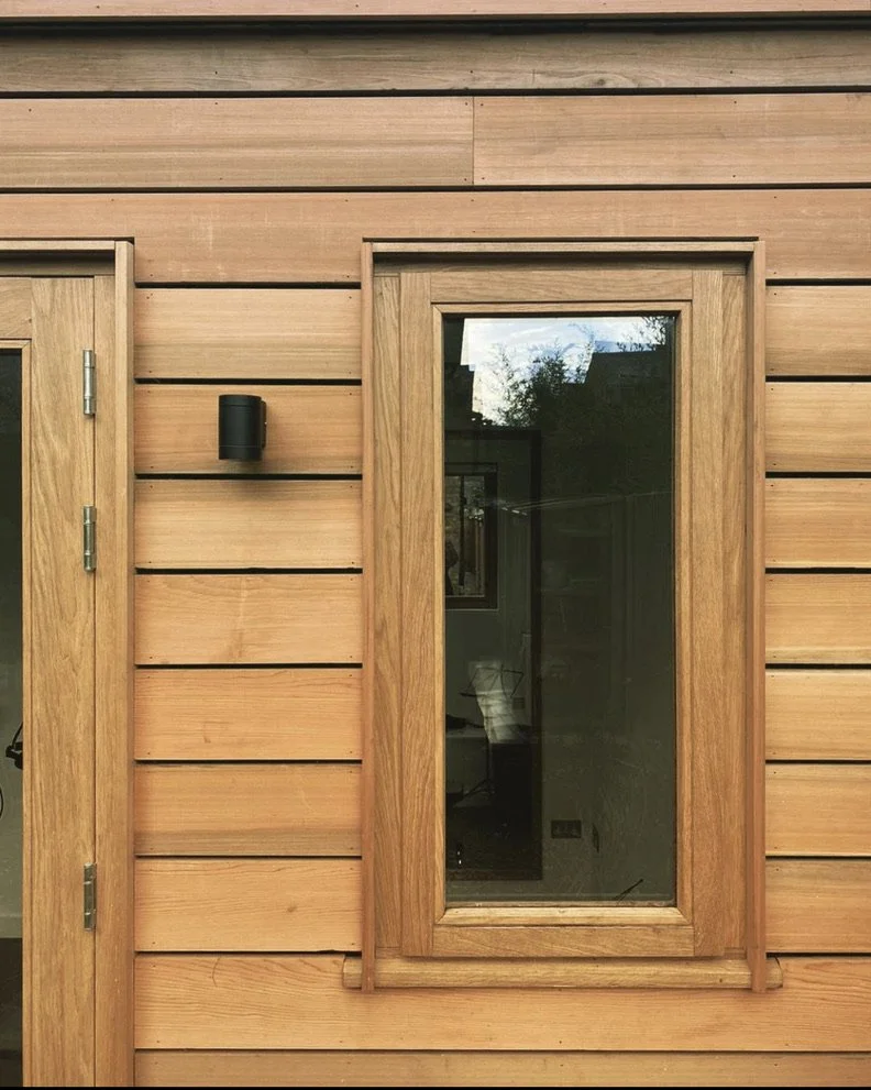 Exterior of a wooden house with horizontal wood siding, a window with a wooden frame, and a black outdoor wall light.
