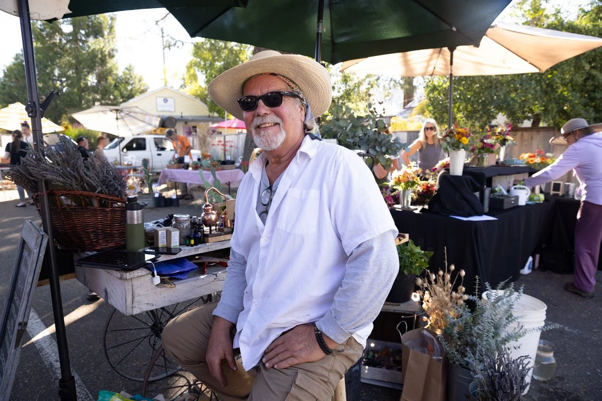 Ron Antone smiling at his Sutter Creek farmers market booth, surrounded by lavender, flowers, and market goods