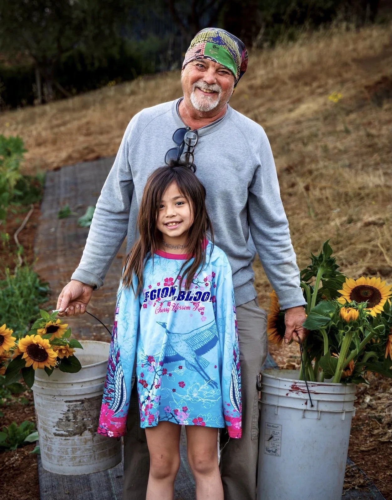 Ron Antone and a young girl beaming beside buckets of freshly picked sunflowers on the farm