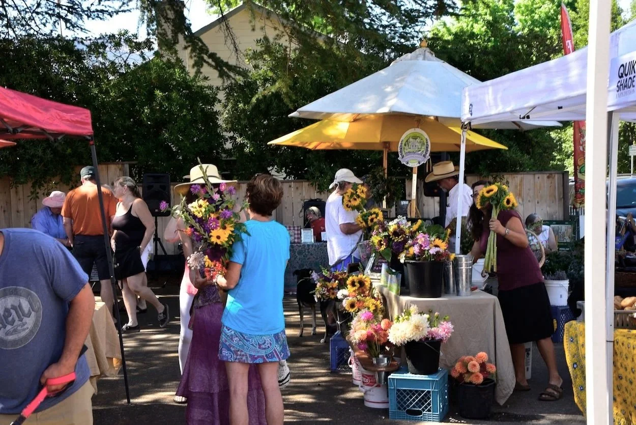 Baskets of dried lavender and sunflower bouquets arranged near an Amador Farmers Market sign