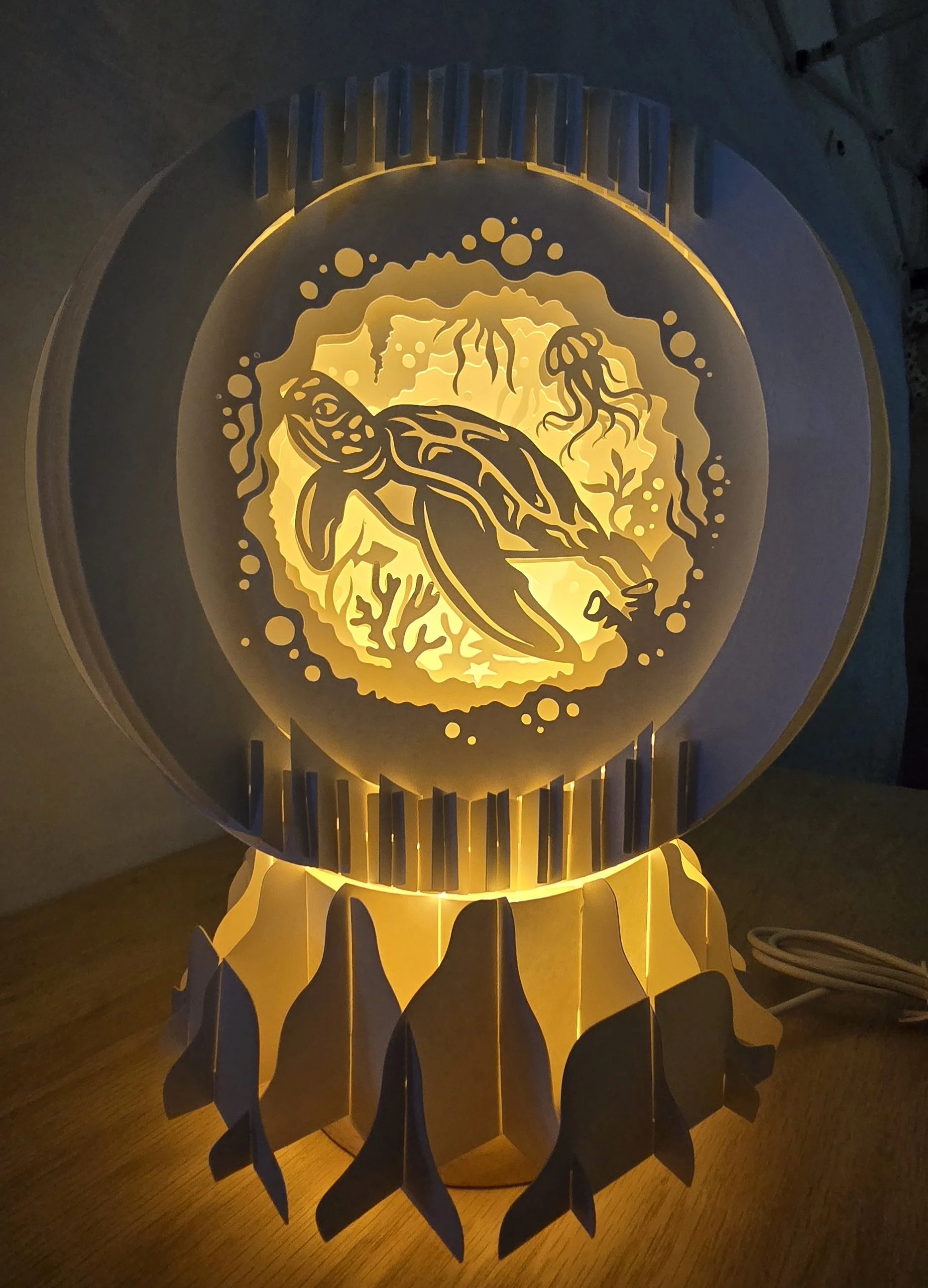 A decorative lamp with an intricate design of a sea turtle, coral, and seaweed, illuminated with warm yellow light, sitting on a wooden surface.