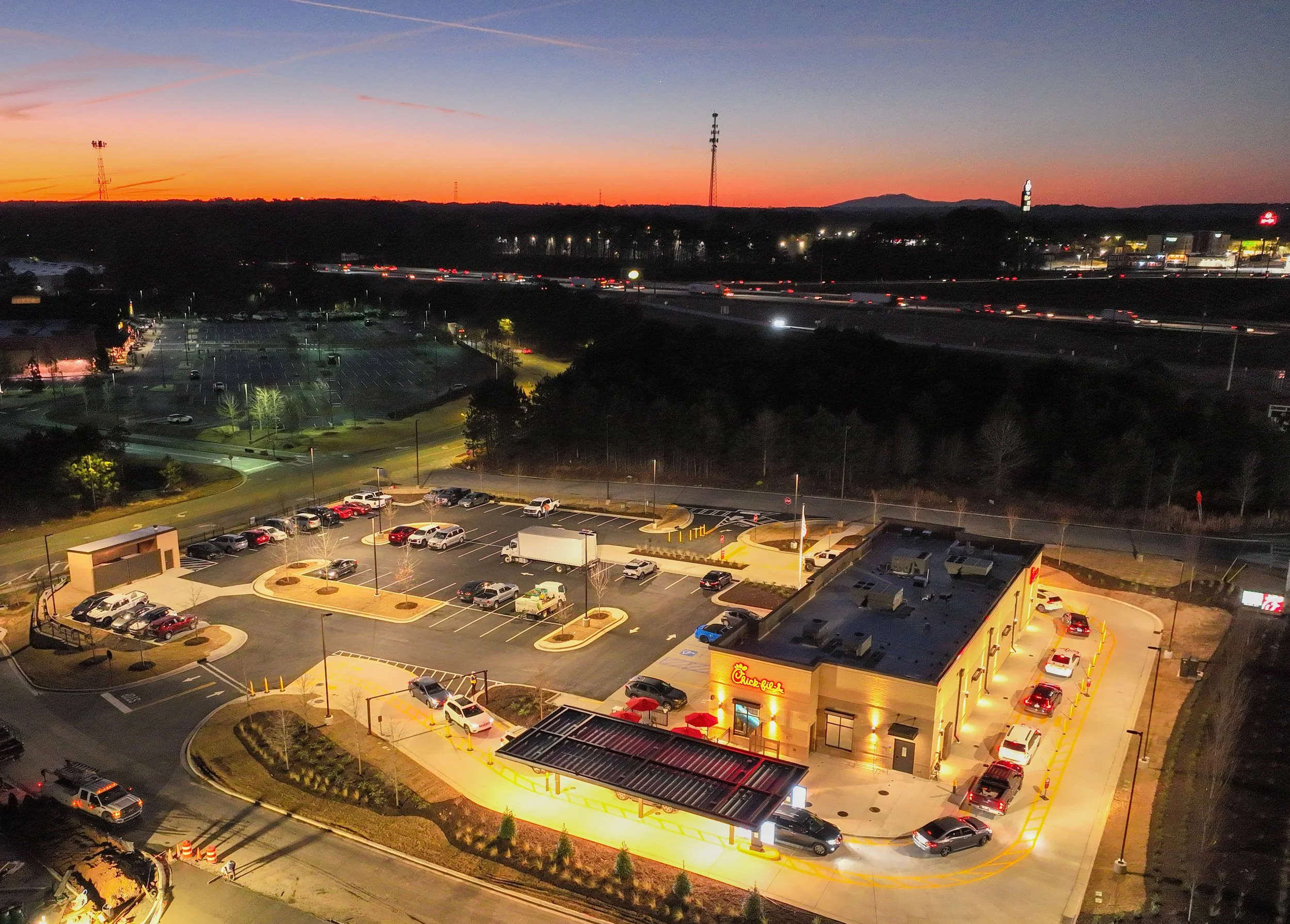 A Chick-fil-A restaurant at dusk with parking lot and nearby highway in the background.