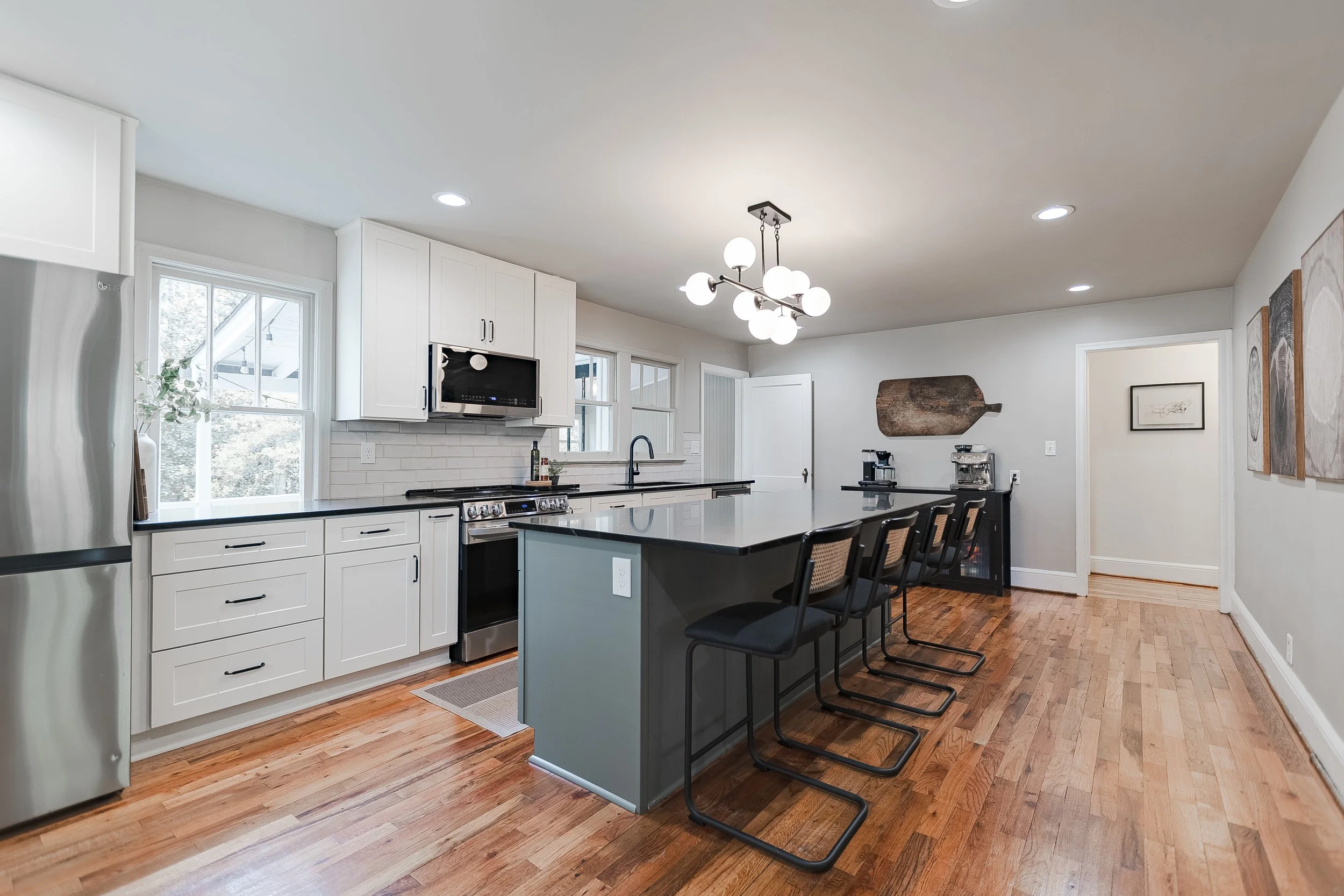 Modern kitchen with white cabinets, black countertops, stainless steel appliances, hardwood floors, bar seating, and minimalist decor.