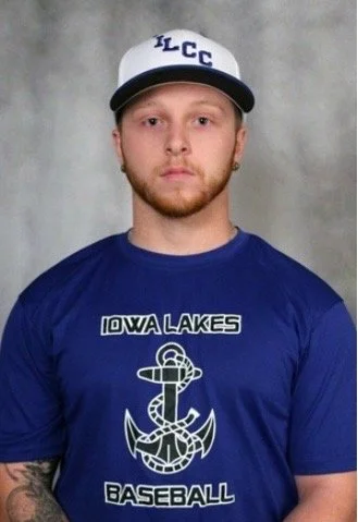 Young man wearing a white cap with blue letters, a blue Iowa Lakes Baseball t-shirt with an anchor and rope graphic, standing against a neutral background.