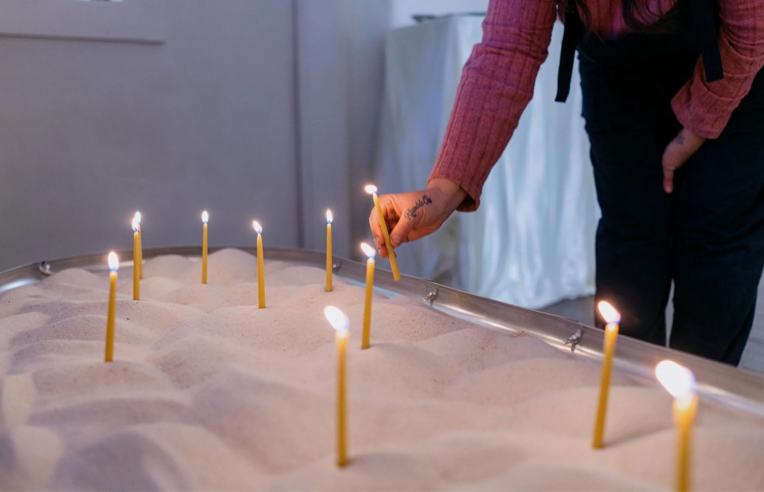 A person is lighting candles on a large cake with sandy-colored icing, possibly for a celebration.