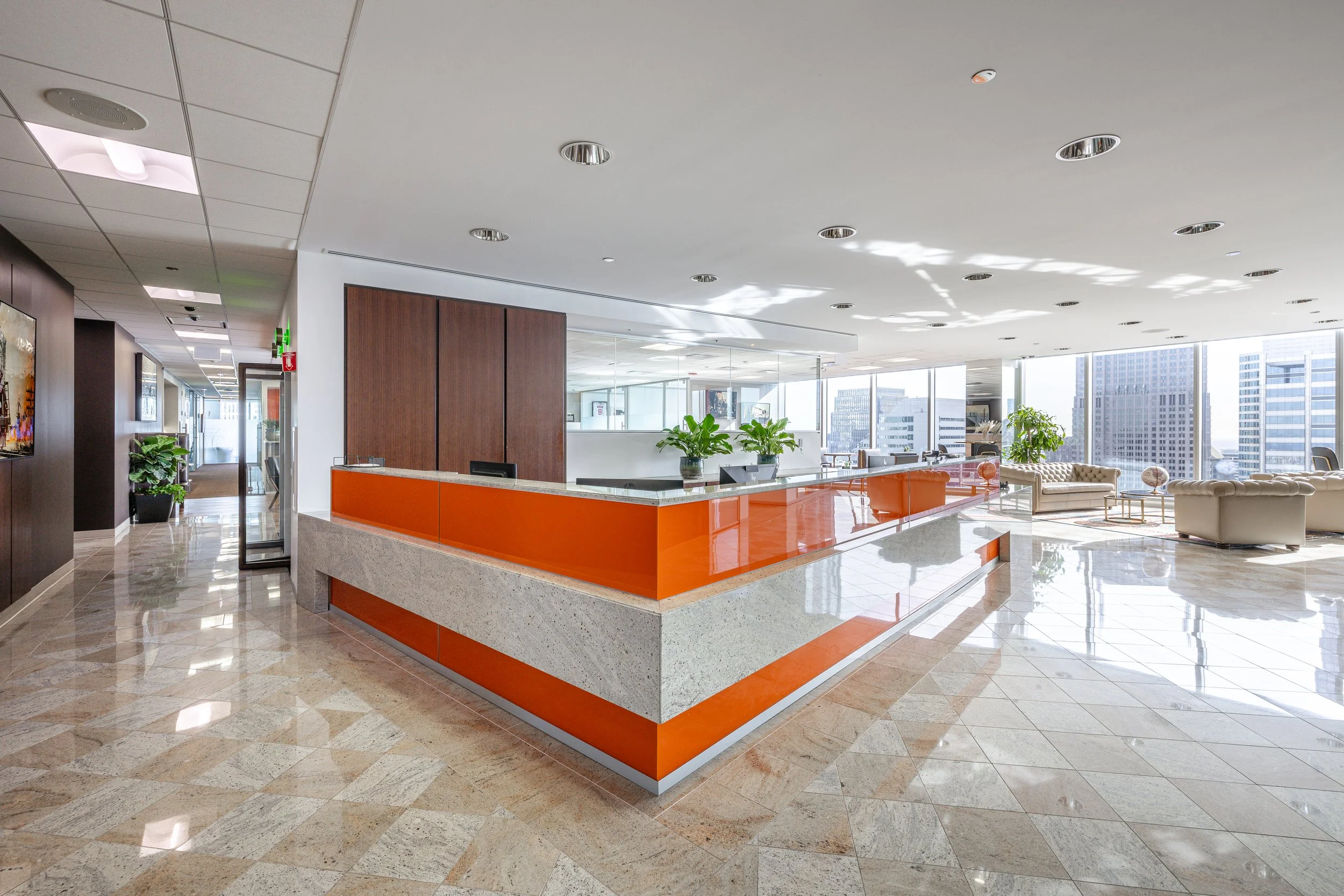 Modern office lobby with a reception desk, large windows, and seating area with white sofas and tables.
